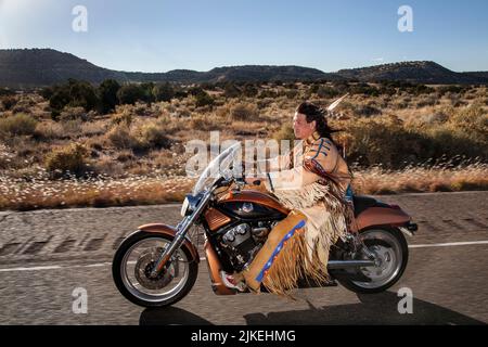 L'uomo nativo americano vestito tradizionalmente (Arapahoe) guida la motocicletta Harley Davidson lungo l'autostrada di campagna Foto Stock