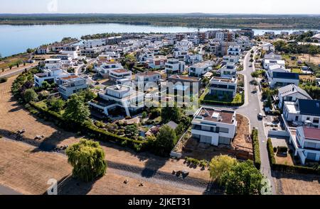 Zwenkau, Germania. 19th luglio 2022. Un porto e nuovi edifici residenziali sono stati costruiti a Capo Zwenkau sul lago omonimo. L'ex miniera di lignite a cielo aperto di Zwenkau ha dato origine al più grande lago della regione di Lipsia, che copre un'area di quasi 10 chilometri quadrati. Dal 2011 è in costruzione un nuovo quartiere sulla riva Zwenkau, che offre spazio per vivere e lavorare. (Vista aerea con drone) Credit: Jan Woitas/dpa/ZB/dpa/Alamy Live News Foto Stock