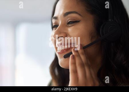 Come posso essere d'aiuto oggi. Una giovane donna d'affari che indossa una cuffia mentre lavora in un call center. Foto Stock