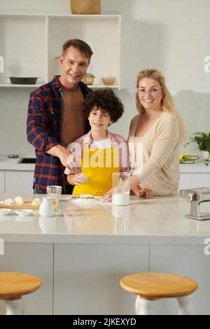 I genitori felici che aiutano il figlio con la preparazione della pasta per la cena Foto Stock