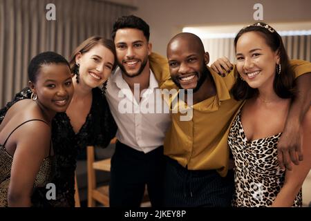 Weve è sempre stato più familiare che amici. Un gruppo di amici diversi in piedi con le braccia l'uno intorno all'altro durante una cena di Capodanno. Foto Stock