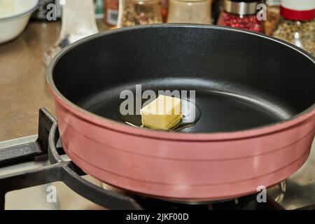 Un pezzo di burro viene sciolto in padella prima di cuocere. Foto Stock