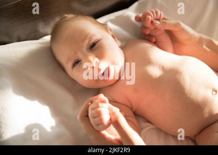 Un bambino piccolo divertente che si trova su un letto e che mostra la sua lingua Foto Stock