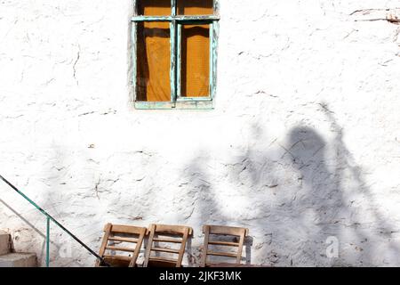 Vecchia finestra di legno nel muro di una vecchia casa. Sedie in legno Foto Stock