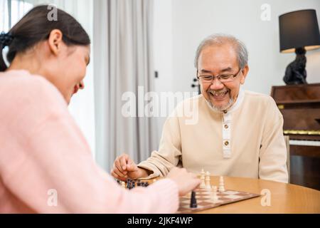 Sorridente anziano che si diverte giocando a scacchi con bella figlia a casa, infermiere caregiver in casa di cura per il tempo libero, felice attivo ritiro Foto Stock