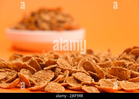 Primo piano di fiocchi di grano su sfondo arancione, veloce cereali salubre colazioni Foto Stock