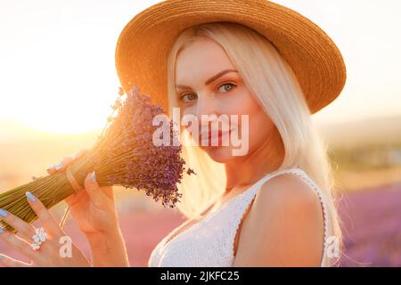 Ritratto o ragazza bionda affascinante puzza fiori di lavanda in campo di lavanda Foto Stock