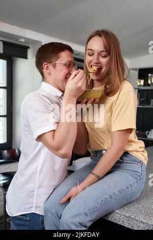 Sorridendo amorevole marito che alimenta moglie, giovane coppia che gode momento tenero, data romantica, divertirsi, mangiare cucina giapponese, felice famiglia spesa Foto Stock