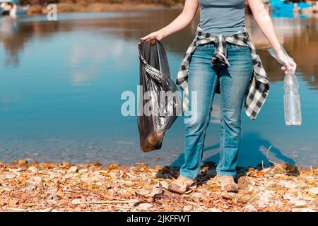 Ecologia e raccolta rifiuti. Donna volontaria con un sacco di rifiuti nelle sue mani, impegnato nella raccolta di rifiuti sul lago o sul mare. Primo piano. Foto Stock