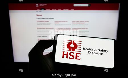 Persona che tiene il cellulare con il logo dell'agenzia britannica Health and Safety Executive (HSE) sullo schermo di fronte alla pagina web. Mettere a fuoco sul display del telefono. Foto Stock