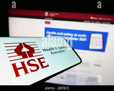 Telefono cellulare con il logo dell'agenzia britannica Health and Safety Executive (HSE) sullo schermo di fronte al sito Web. Mettere a fuoco sulla sinistra del display del telefono. Foto Stock