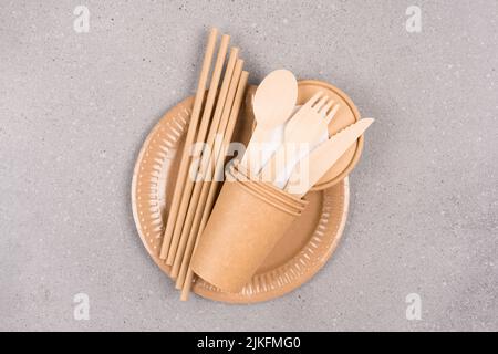 Concetto di catering e utensili ecologici - piatti e tazze di carta, posate in legno e cannucce da bere su sfondo grigio di cemento con spazio per la copia per te Foto Stock