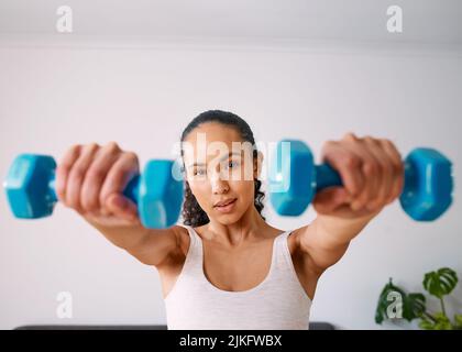 Una giovane donna seria solleva piccoli pesi per diventare forte a casa Foto Stock