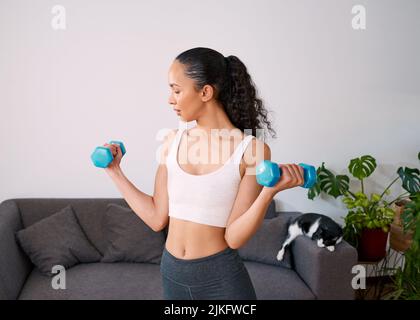 Una giovane donna seria solleva piccoli pesi per diventare forte a casa Foto Stock