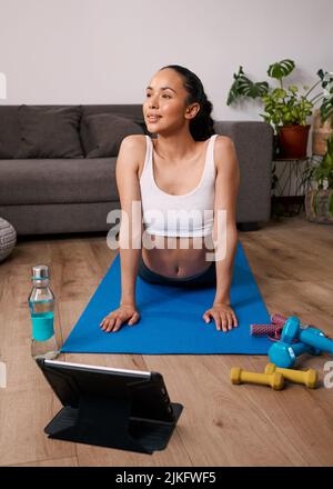 Una giovane donna si allunga verso l'alto guardando il cane durante l'allenamento virtuale a casa Foto Stock