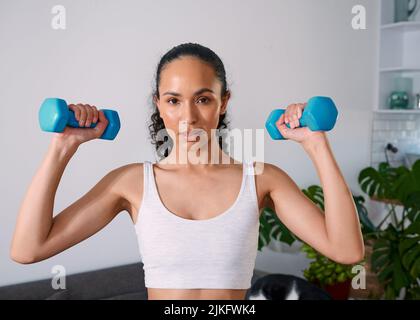 Una giovane donna seria solleva piccoli pesi per diventare forte a casa Foto Stock