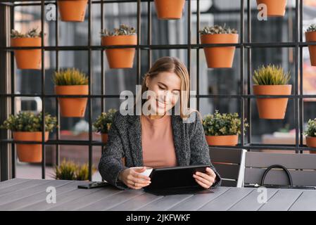 Una giovane studentessa felice di successo fa una video chat mentre si siede sulla terrazza di un caffè all'aperto Foto Stock