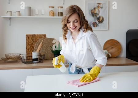 Casalinga in guanti gialli pulisce il tavolo da cucina Foto Stock