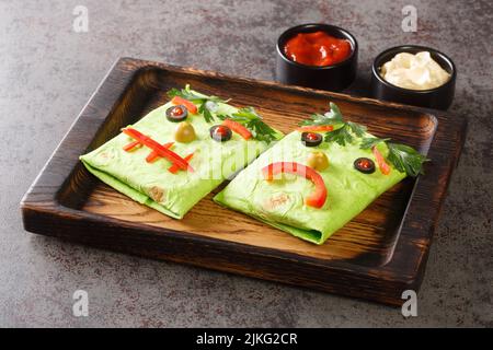 Halloween Monster avvolge burrito sandwich con faccia divertente su un vassoio di legno sul tavolo. Orizzontale Foto Stock