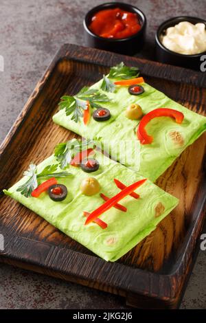 Festa di Halloween burritos mostro cibo per bambini con salse su un vassoio di legno sul tavolo. Verticale Foto Stock