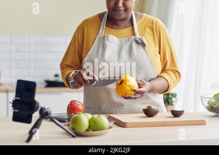 Scatto corto di giovane donna nera che cucinano pasto sano in cucina e registrare video con smartphone, spazio copia Foto Stock