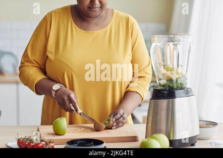 Primo piano di donna nera tagliare frutta mentre si fa pasto sano in cucina e filmare video di cucina, copia spazio Foto Stock