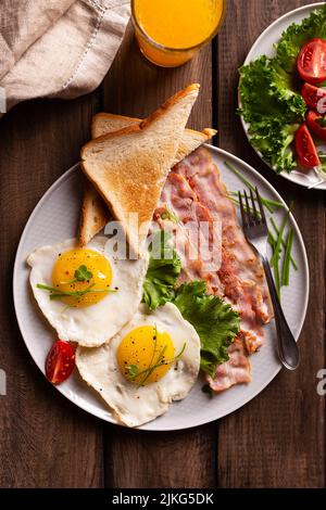 Colazione all'americana con uova e pancetta in un piatto su un tavolo di legno. Vista dall'alto del cibo sano Foto Stock