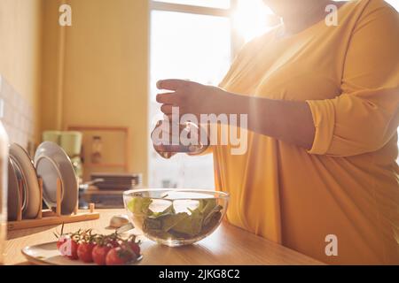 Primo piano di donna nera irriconoscibile che cucinano pasto sano in cucina illuminata dalla luce del sole, spazio copia Foto Stock