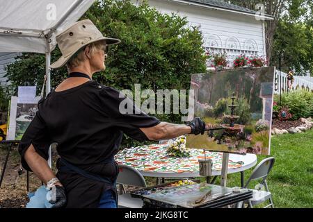 Donna artista al lavoro che dipinge una scena di una fontana in un giardino di fiori. Foto Stock