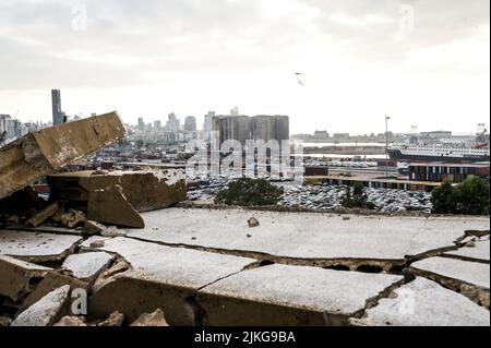 Beirut, Libano, 31 luglio 2022. Elicotteri d'acqua al lavoro dopo il crollo di due silos dal blocco nord dei silos di grano di Beirut Port, a seguito di oltre due settimane di incendi di grano fermentato all'interno della struttura gravemente danneggiata nel 4 agosto 2020 Beirut Port Blast, Visto qui attraverso le macerie di un edificio danneggiato dall'esplosione che è rimasto intatto nei due anni dall'esplosione. Foto Stock