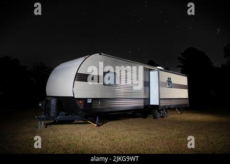 Rimorchio da campeggio su un punto erboso con stelle luminose sopra Foto Stock