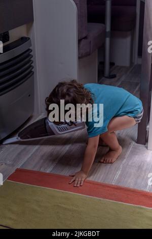 Il bambino, simpatico e diligente, pulisce la roulotte con un aspirapolvere. Foto Stock