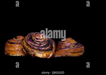 Immagine di tre ciambelle con semi di papavero, cannella e ciliegie su sfondo nero Foto Stock