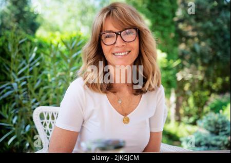 Primo piano ritratto di felice donna di mezza età seduta in una poltrona mentre si rilassa nel cortile. Foto Stock