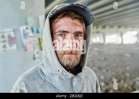 Primo piano di un uomo senza tetto con volto sporco in abiti strappati guardando la macchina fotografica in piedi all'aperto Foto Stock