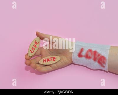 Una mano di un uomo che tiene le tavole di legno con le parole 'AMORE' e 'ODIO' con una garza bianca sul polso Foto Stock