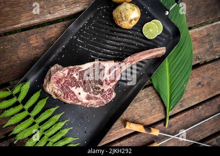 Un pezzo di bistecca di manzo crudo su un osso con erbe e spezie dall'alto Foto Stock