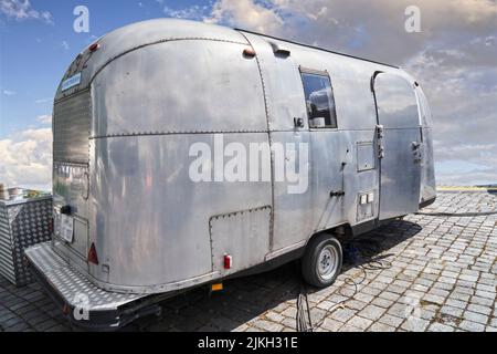 Airstream camper, vecchio esempio leggermente intemperiato del famoso veicolo americano fatto di piastre rivettate in alluminio ad Hannover, Germania, 23 luglio 2022 Foto Stock