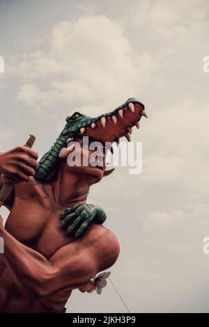 Un tiro a basso angolo di una figura di cera d'uomo con un coccodrillo contro un cielo nuvoloso in un parco divertimenti Foto Stock