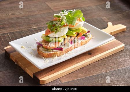 Un primo piano di bruschetta italiana con pomodori, avocado, uova in camicia e rucola di cipolle Foto Stock