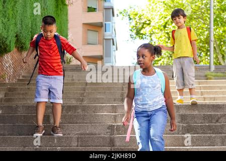 bambini multietnici con zaini sulla strada per la scuola. Concetto di ritorno a scuola. Gruppo di bambini multietnici Foto Stock