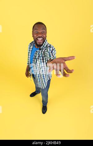 Il ragazzo nero mostra un oggetto invisibile che urla la mano stretching, sfondo giallo Foto Stock