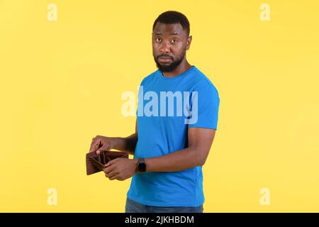 Unhappy Black Man mostrando portafoglio vuoto che ha problemi finanziari, Studio Foto Stock