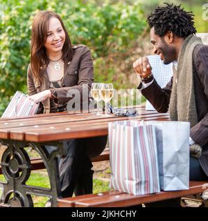 Shopping a Londra; shopping break. Una giovane coppia di corse miste condivide un drink dopo una giornata di shopping. Da una serie di immagini con gli stessi caratteri. Foto Stock