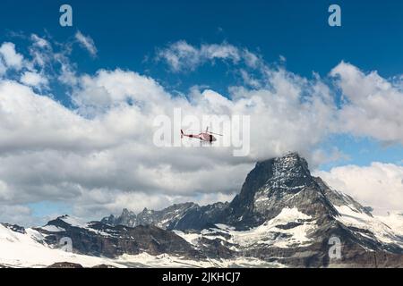 Cervino nelle Alpi svizzere. Una nuvola bianca si trova sulla montagna sullo sfondo, un elicottero rosso da piacere vola. Foto Stock