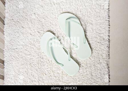 Abbina infradito color menta piperita su tappeto bianco in bagno. Concetto di pulizia e cura personale, vista dall'alto Foto Stock