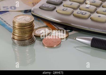 Una pila di monete in euro e una calcolatrice con banconote in euro macerate Foto Stock