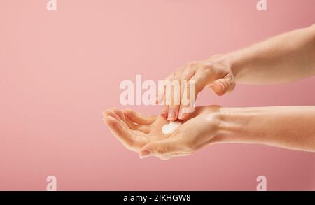 Una donna che applica crema a portata di mano su sfondo rosa isolato Foto Stock