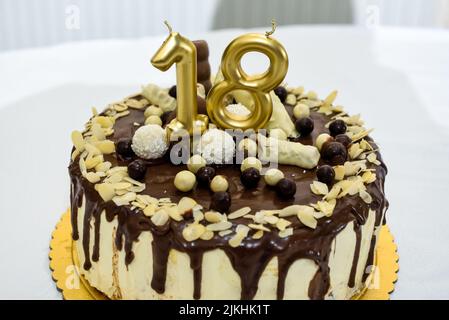 Una torta di festa con candele d'oro per un diciottesimo compleanno o anniversario di celebrazione su un tavolo bianco Foto Stock