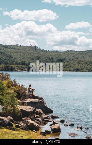 Un giovane caucasico seduto sulla roccia e guardando il mare Foto Stock